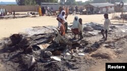 FILE - People stand amid the damage at a camp for displaced people after an attack by suspected members of the Islamist Boko Haram insurgency in Dalori, Nigeria, Nov. 1, 2018. 