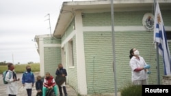 Graciela Villareal, asistente escolar, iza la bandera nacional en la escuela rural 30 en San José, Uruguay, el 22 de abril de 2020.