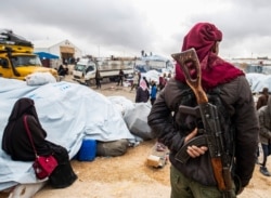 FILE - A member of Kurdish security forces watches as families load their belongings onto trucks before leaving the Kurdish-run al-Hol camp, in the al-Hasakeh governorate in northeastern Syria, Nov. 16, 2020.
