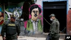 FILE - Police officers stand in front of a mural depicting the late drug kingpin Pablo Escobar, in the area known as El Bronx in downtown Bogota, Colombia, May 30, 2016. The area has been plagued by drug addicts and prostitution, including girls forced into sexual servitude.