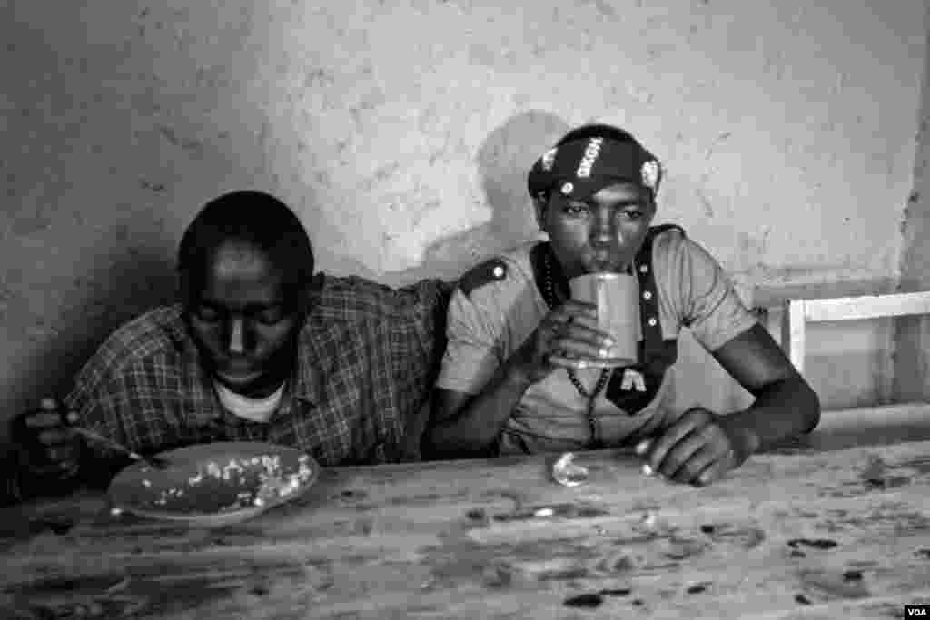 Vansing (right), drinks while he shares a meal with his friend Nshizirungu Amos, age 20. Vansing knew Nshizirungu Amos from an orphanage. Vansing says, "Life in Giblioso is like jail, but we have to share." (Hamada Elrasam for VOA)