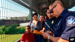 ARCHIVO - Agentes de la Patrulla Fronteriza y Aduanas de EE. UU. procesan a una familia cubana, cuyo turno había sido llamado para cruzar a EE. UU. y solicitar asilo, en un puente internacional entre Nuevo Laredo, México, y Laredo, Texas, el 10 de julio de 2019.