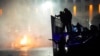 Sebuah mobil polisi terbakar saat polisi anti huru hara bersiap untuk menghentikan pengunjuk rasa di pusat kota Almaty, Kazakhstan, 5 Januari 2022. (Foto: AP)