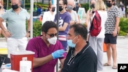 Carlos Anacleto, a la derecha, cierra los ojos mientras recibe una inyección de la vacuna Pfizer contra el COVID-19 de la enfermera Jorge Tase, mientras otros esperan su turno, el 4 de agosto de 2021, en Miami Beach, Florida.