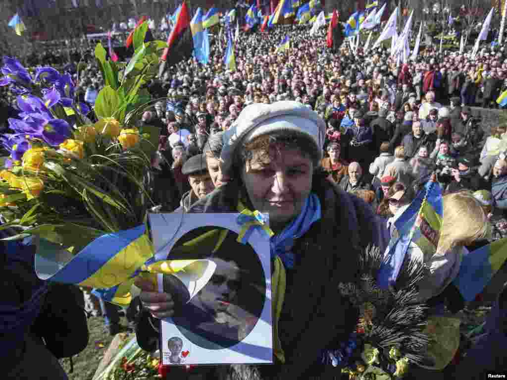 A woman holds a portrait of Ukrainian poet Taras Shevchenko while the crowd solemnly commemorates the 200th anniversary of the birth of its greatest poet takes to mark his 200th birthday near a monument of him in central Kyiv, March 9, 2014. 