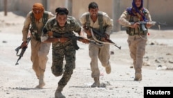 Kurdish fighters from the People's Protection Units (YPG) run across a street in Raqqa, Syria, July 3, 2017. 