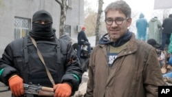 In this photo taken on April 13, 2014, American reporter Simon Ostrovsky, right, stands with a pro-Russian gunman near a police station in the eastern Ukrainian town of Slovyansk. 