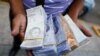 El asistente de un conductor de autobús sostiene billetes de Bolívar, por valor de entre 0,01 y 0,25 dólares estadounidenses, luego de que el Banco Central de Venezuela anunciara que recortará seis ceros de precios, en Caracas.