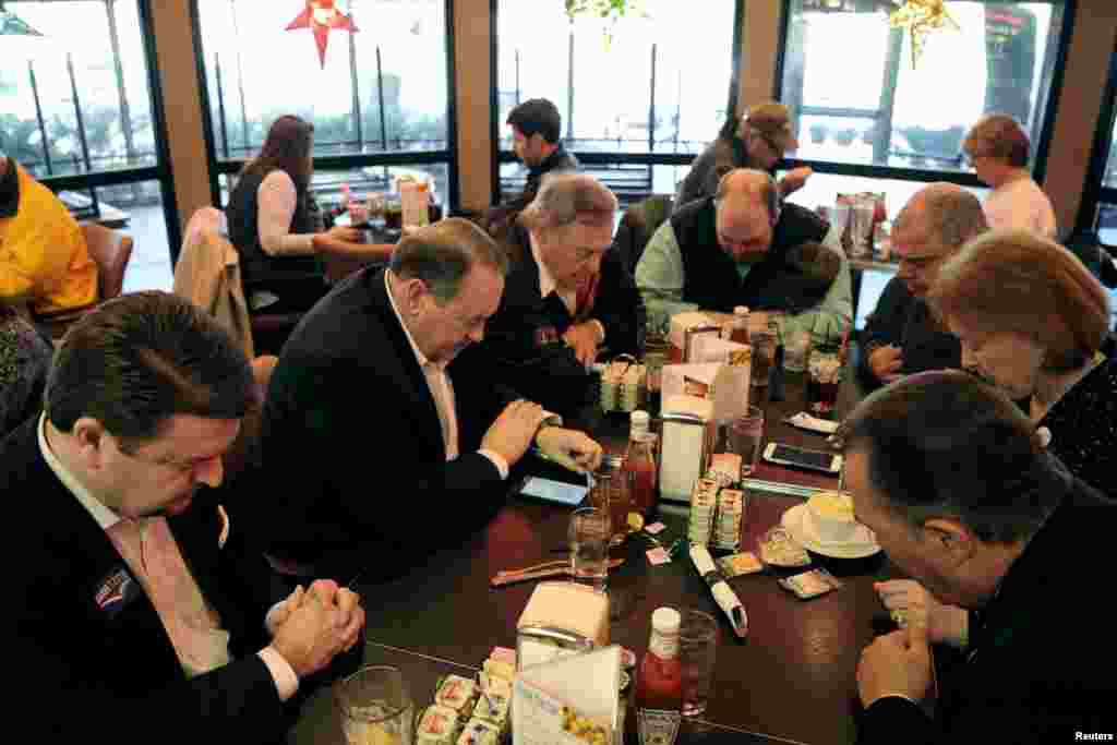 U.S. Republican presidential candidate Mike Huckabee (second from left) prays before lunch with supporters at Drake Diner in Des Moines, Iowa. Feb. 1, 2016.