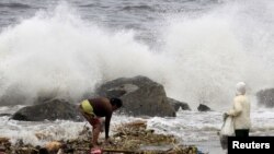 FILE - Residents collect recyclable materials from floating garbage found in the sea, while big waves crash along the coastline due to strong winds brought by Typhoon Goni, locally named as Ineng, at Manila bay, Aug. 22, 2015.