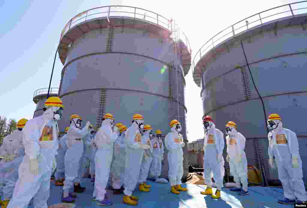 Japan's Prime Minister Shinzo Abe (in red helmet), wearing a protective suit and mask, is briefed about tanks containing radioactive water by Fukushima Daiichi nuclear power plant chief Akira Ono in Okuma, Sept. 19, 2013.