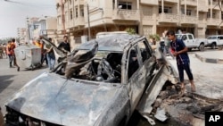 Warga menginspeksi sebuah mobil yang hancur akibat serangan bom dekat pintu gerbang iZona Hijau di Baghdad, Irak (19/3).