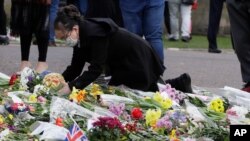 Una mujer coloca una ofrenda floral afuera del Castillo de Windsor en Windsor, Inglaterra, el domingo 11 de abril de 2021, en honor del príncipe Felipe, esposo de la reina Isabel II. 