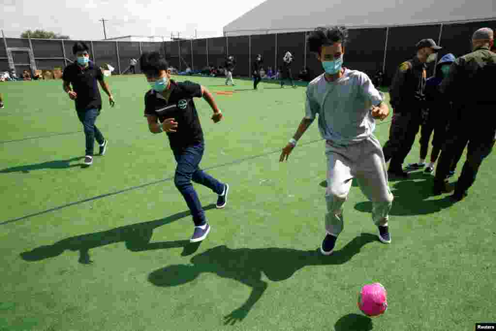 Niños migrantes juegan fútbol en un pequeño terreno dentro del centro de detención.