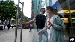 Passers-by wear face masks out of concern for COVID-19 while entering and departing a business, Oct. 14, 2021, in Boston.