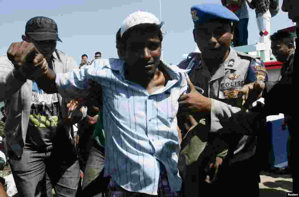 A police officer guides guides an ethnic Rohingya refugee from Burma off a boat that was headed to Australia before he is transported to a temporary shelter in Aceh Besar, April 8, 2013.