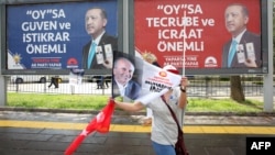 FILE - A supporter of the presidential candidate of Turkey's main opposition Republican People's Party Muharrem Ince waves flags as she walks past election campaign posters for Turkish President Recep Tayyip Erdogan, during an election rally in Ankara, June 22, 2018.