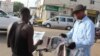 A man buys a newspaper from a street vendor in Westfield, Banjul, Gambia, June 7, 2017. (S.Christensen/VOA)