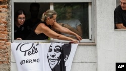 Una bandera cuelga de la casa de la madre de Pelé mientras los restos del difunto, un grande del fútbol brasileño. son llevados del estadio Vila Belmiro al cementerio durante su cortejo fúnebre en Santos, Brasil, el 3 de enero de 2023.