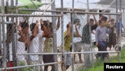 FILE - Asylum-seekers look through a fence at the Manus Island detention center in Papua New Guinea, March 21, 2014. 