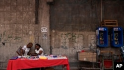Dos mujeres hablan mientras una muestra sus productos a la venta en una mesa en la acera de la Avenida Central en Ciudad de Panamá, el 26 de julio de 2022. 