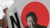 A South Korean man stands next to a sign with a picture of the Japanese Prime Minister Shinzo Abe during a rally to denounce Japan's trade restrictions on South Korea in Seoul, South Korea, Aug. 8, 2019.