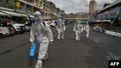 FILE - Workers wearing personal protective equipment (PPE) carry disinfectant to be sprayed at the Orussey market, after it was temporarily closed following a few vendors testing positive for the Covid-19 coronavirus, in Phnom Penh on April 4, 2021. (AFP)