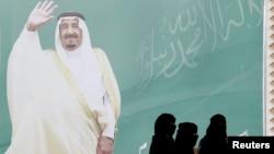 FILE - Women walk past a poster of Saudi Arabia's King Salman bin Abdulaziz Al Saud during Janadriyah Cultural Festival on the outskirts of Riyadh, Saudi Arabia Feb. 12, 2018.