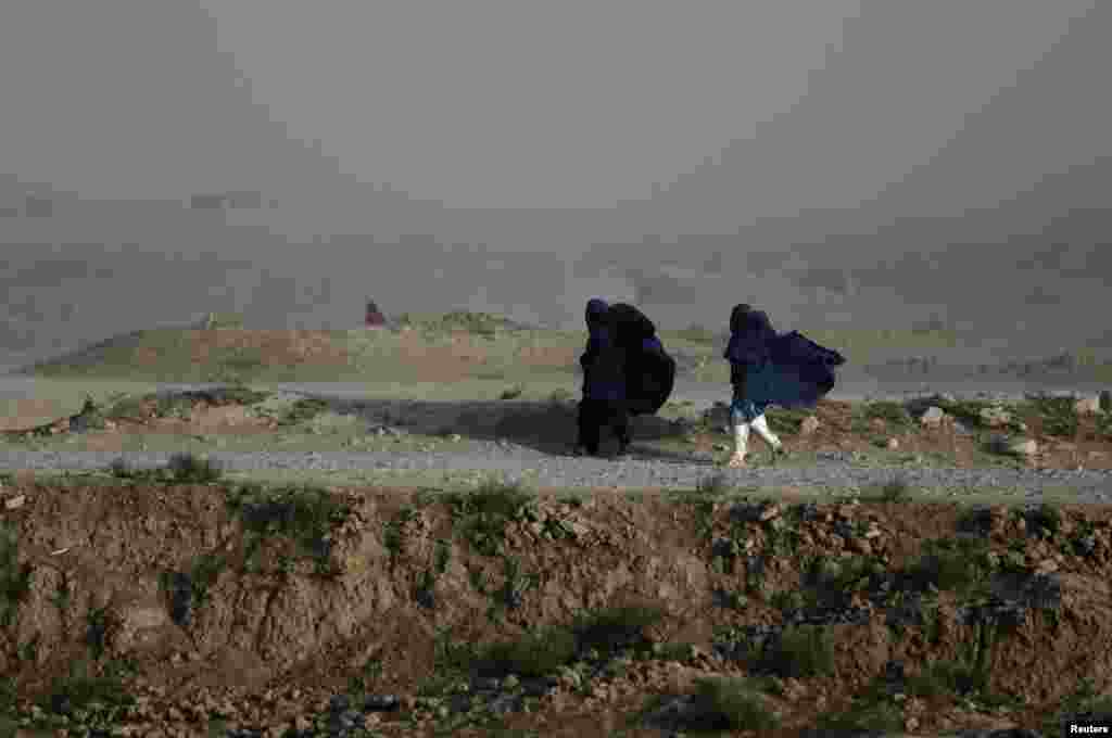 Dua orang perempuan Afghanistan berjalan di tengah angin kencang di pinggiran ibukota Kabul.