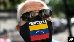 Un hombre usa una mascarilla con la bandera de Venezuela, mientras espera para llenar el tanque de su automóvil en una estación en Caracas, Venezuela. Mayo 25, 2021. Foto: AP.