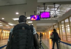 FILE - Passengers from an Ethiopian Airlines flight from Addis Ababa walk past a thermal imaging camera checking for signs of fever upon their arrival at the Jomo Kenyatta International Airport in Nairobi, Kenya, Feb. 6, 2020.