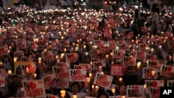 Protesters hold candles and signs during a rally denouncing Japanese Prime Minister Shinzo Abe and also demanding the South Korean government cancel its GSOMIA agreement with Japan, in downtown Seoul, South Korea, Aug. 15, 2019.