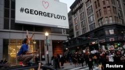 Personas gritan desde un vehículo, en Boston, Massachusetss, mientras otros marchan bajo un rótulo con el nombre de George Floyd, quien murió bajo custodia de la policía de Minneapolis. 