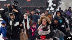 FILE - A group of migrants move through snow toward a train station to be transferred to Austria, near the border with Croatia, in Dobova, Slovenia, Jan. 3, 2016.