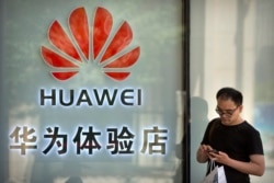 FILE - A man uses his smartphone outside of a shop selling Huawei products at a shopping mall in Beijing, China, May 29, 2019.