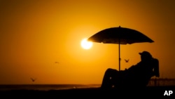 ARCHIVO - Una persona descansa bajo uns sombrilla de playa a la puesta del sol el 12 de septiembre de 2023 en Newport Beach, California, en uno de los veranos más calientes en la zona.