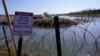 ARCHIVO - Migrantes cruzan el Río Grande hacia EEUU desde México detrás de un alambre de púas y un letrero que advierte que es peligroso e ilegal cruzar, el 3 de enero de 2024, en Eagle Pass, Texas.