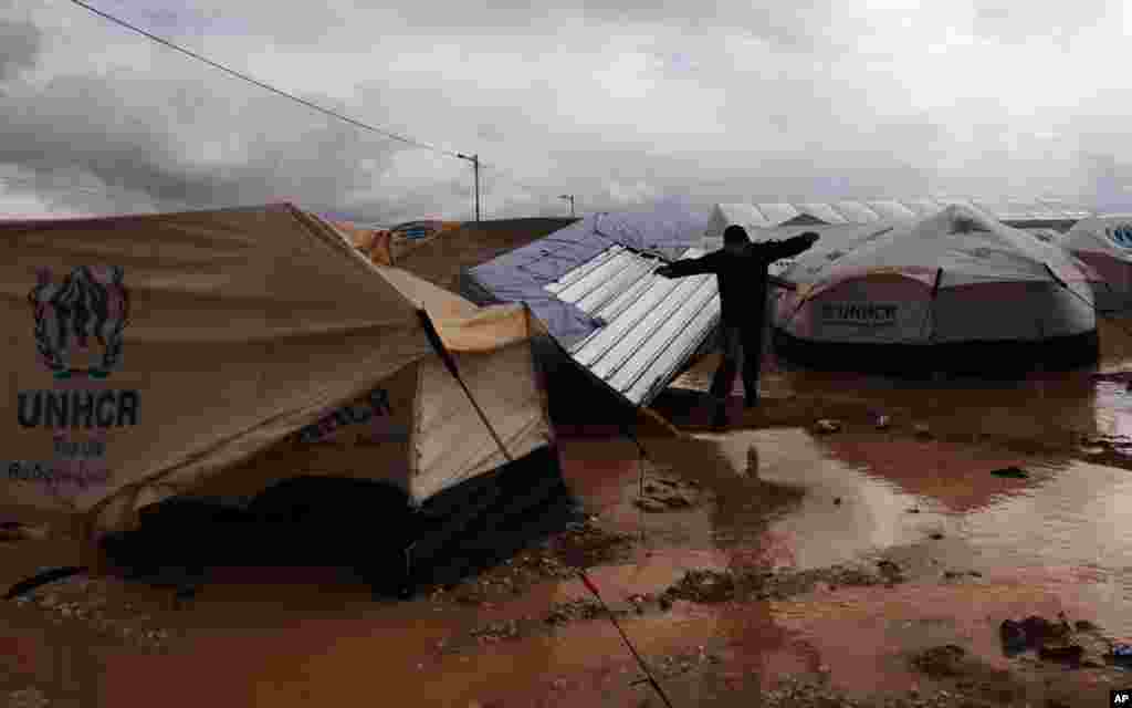 A Syrian refugee man jumps to avoid muddy water near his tent, at Zaatari refugee camp, near the Syrian border in Mafraq, Jordan, January 9, 2013.
