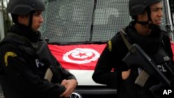 FILE - A Tunisian national flag is seen on a police vehicle as policemen stand guard following an attack by gunmen, claimed later by Islamic State, in Tunis, Tunisia, March 20, 2015.