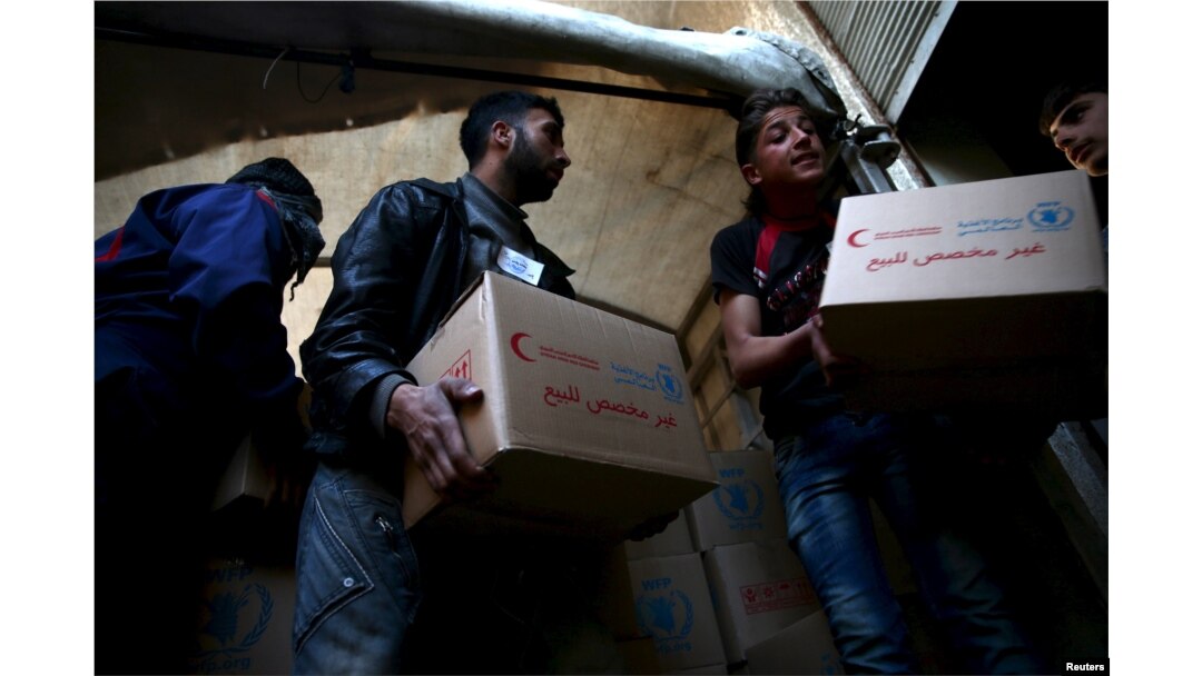 Men unload aid boxes from a Red Crescent aid convoy in the rebel held besieged town of Jesreen, in the eastern Damascus suburb of Ghouta, Syria, March 7, 2016.
