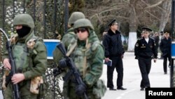 Armed men (L), believed to be Russian servicemen, stand guard outside Ukraine's naval headquarters after it was taken over by pro-Russian forces, as Russian naval officers (R) are seen in the background, in Sevastopol, March 19, 2014.