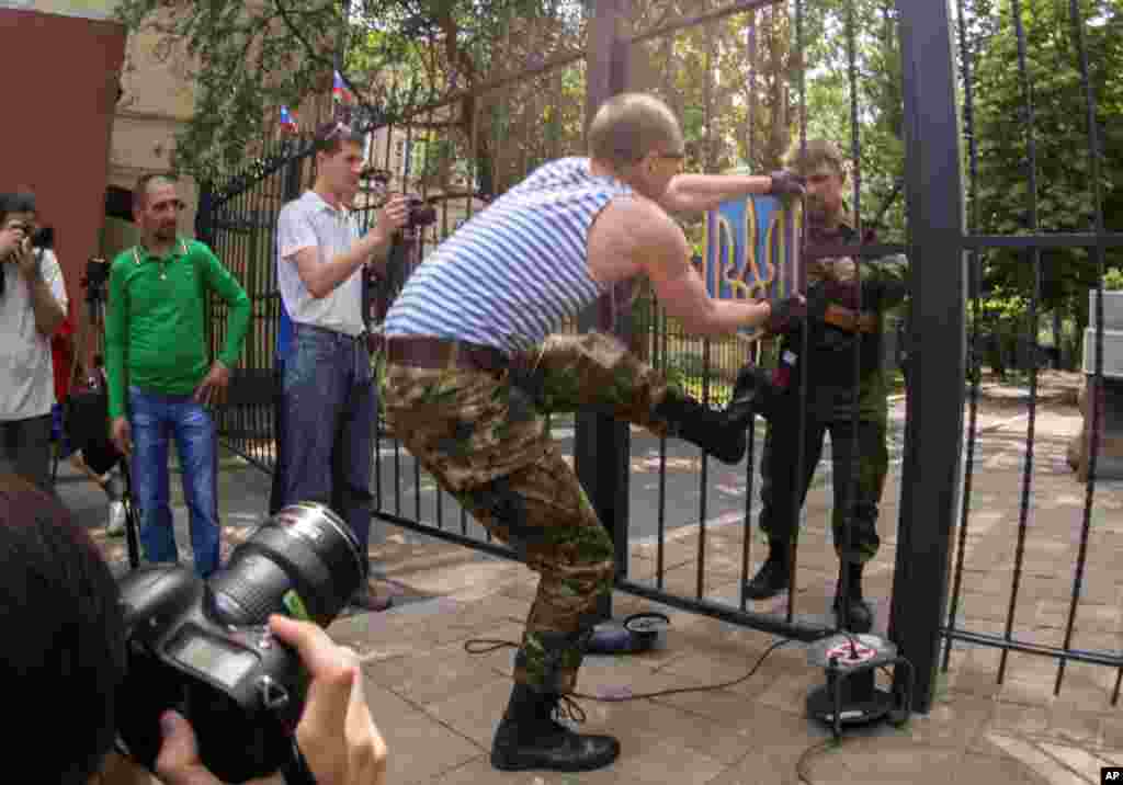 A pro-Russian man tries to remove a Ukrainian national emblem from the gates to the city administration headquarters in Luhansk, Ukraine, June 9, 2014.