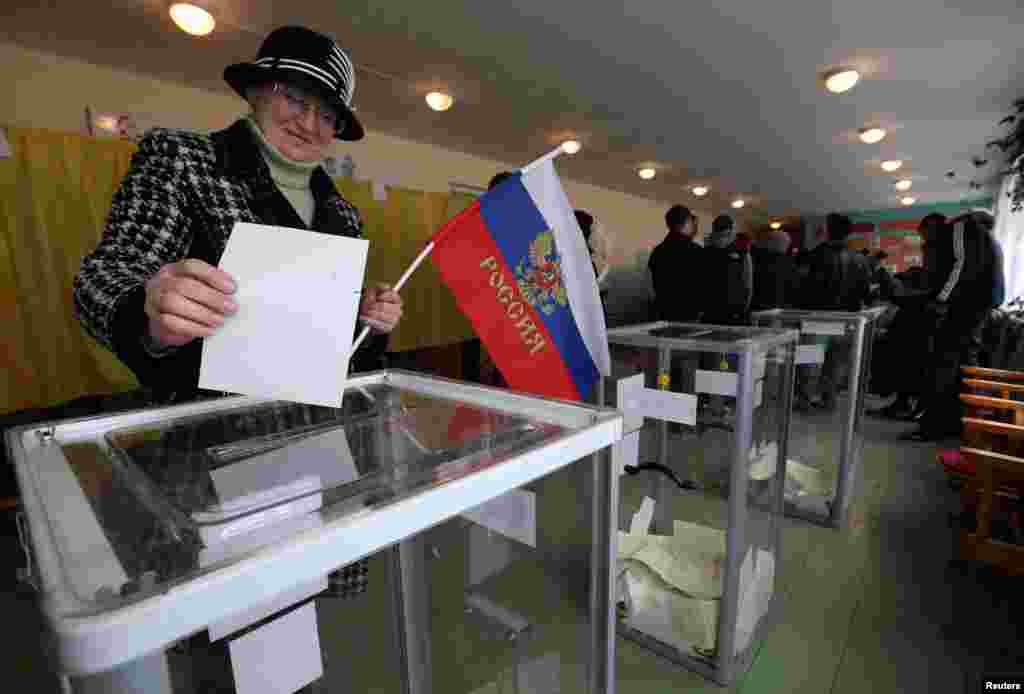 A woman holds a Russian flag as she casts her ballot during the referendum on the status of Ukraine's Crimea region at a polling station in Bakhchisaray, Crimea, Ukraine, March 16, 2014.