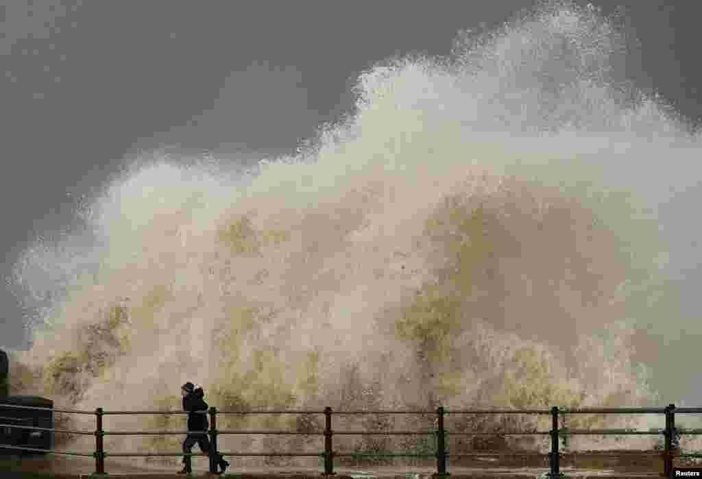 Seorang perempuan berusaha menghindari hantaman ombak di pinggir pantai di New Brighton, Inggris.