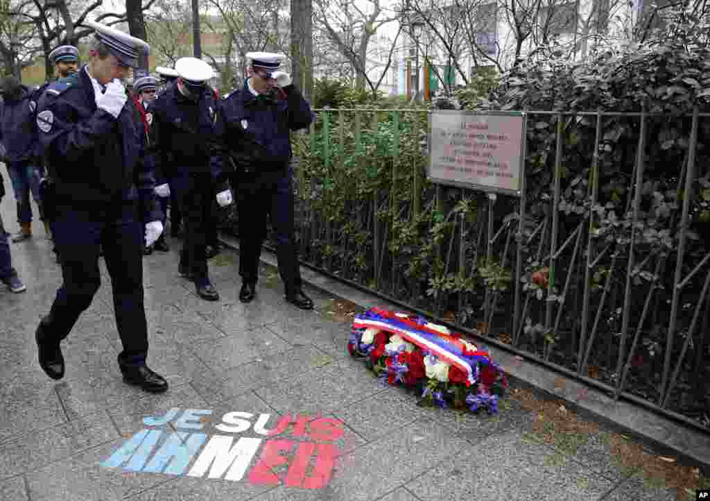 Policemen walk past spray paint on the sidewalk reading: "Je suis Ahmed," or "I am Ahmed," in the red, white and blue of the French flag near a plaque commemorating late police officer Ahmed Merabet in Paris, Tuesday Jan. 5, 2016.