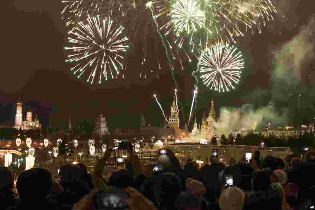 2018年1月1日，在俄罗斯莫斯科举行的新年庆祝活动中，烟花爆竹在克里姆林宫上空怒放，人们仰望和拍照。新年是俄罗斯的主要馈赠节日。