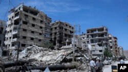 People stand in front of damaged buildings, in the town of Douma, the site of a suspected chemical weapons attack, near Damascus, Syria, April 16, 2018. 