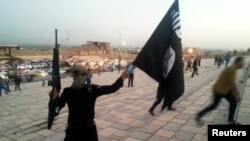 A fighter of the Islamic State of Iraq and the Levant (ISIL) holds an ISIL flag and a weapon on a street in the city of Mosul, June 23, 2014.