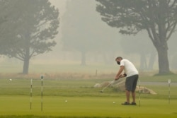 A golfer wears a face mask as he practices his putting at the smoke-shrouded Lake Tahoe Golf Course in South Lake Tahoe, Calif., Aug. 24, 2021.