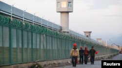 FILE - Workers walk by the perimeter fence of what is officially known as a vocational skills education center in Dabancheng in Xinjiang Uighur Autonomous Region, China, Sept. 4, 2018. 